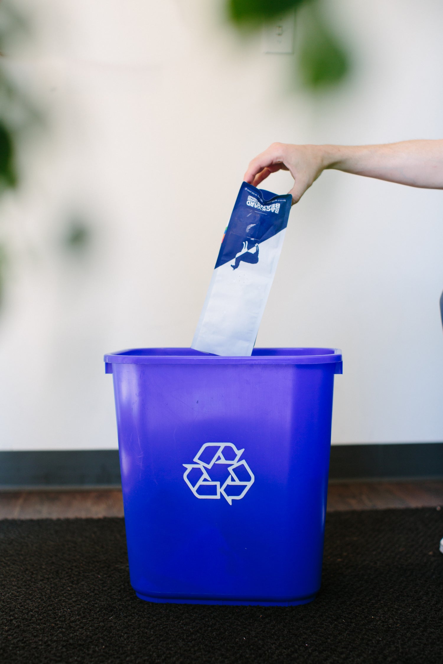 A hand is dropping a coffee bag into a recycling bin. 