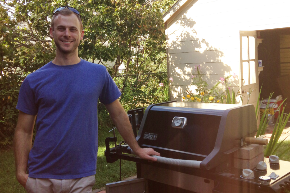Man in a blue shirt standing next to a barbecue grill outdoors