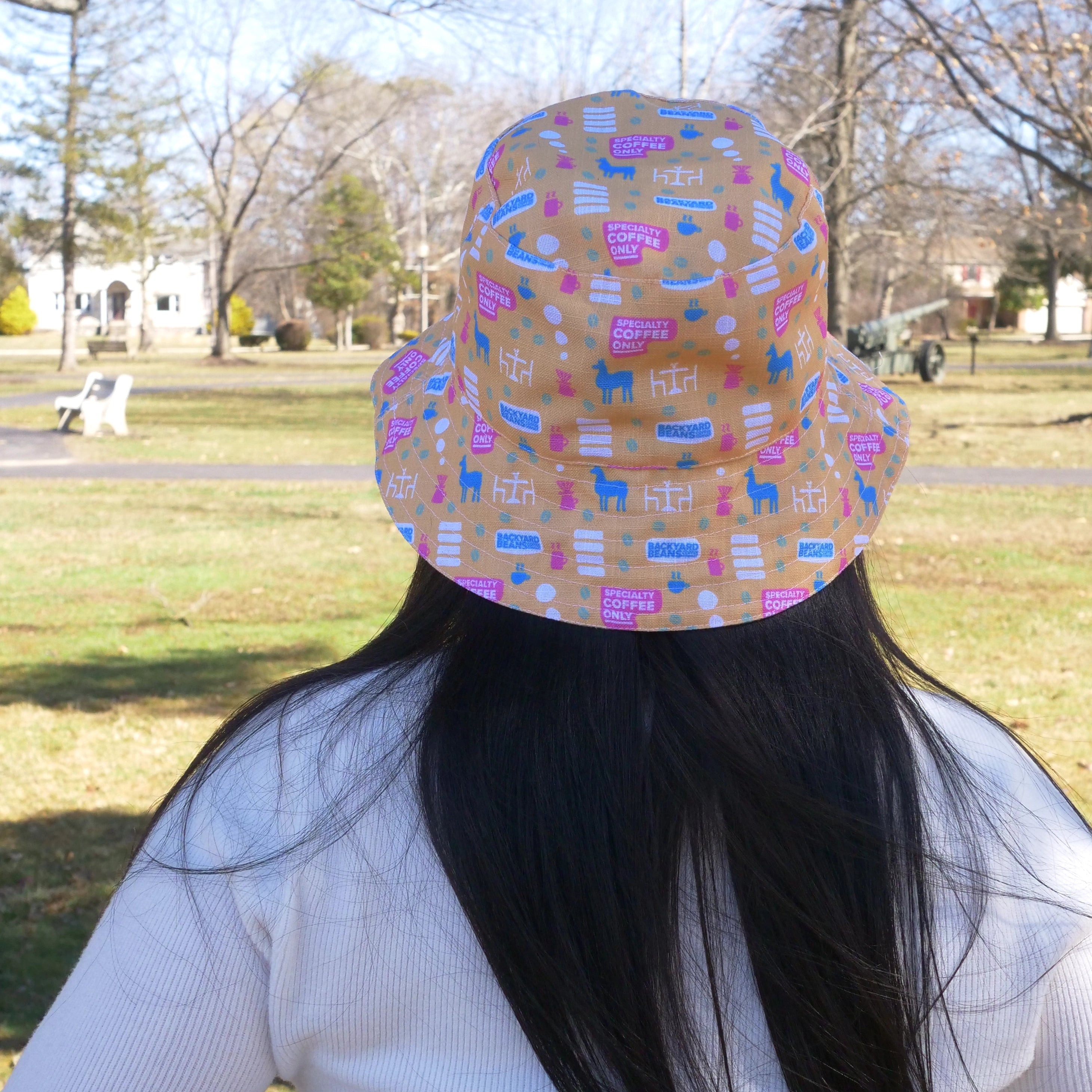 Person wearing a colorful patterned bucket hat outdoors in a park.