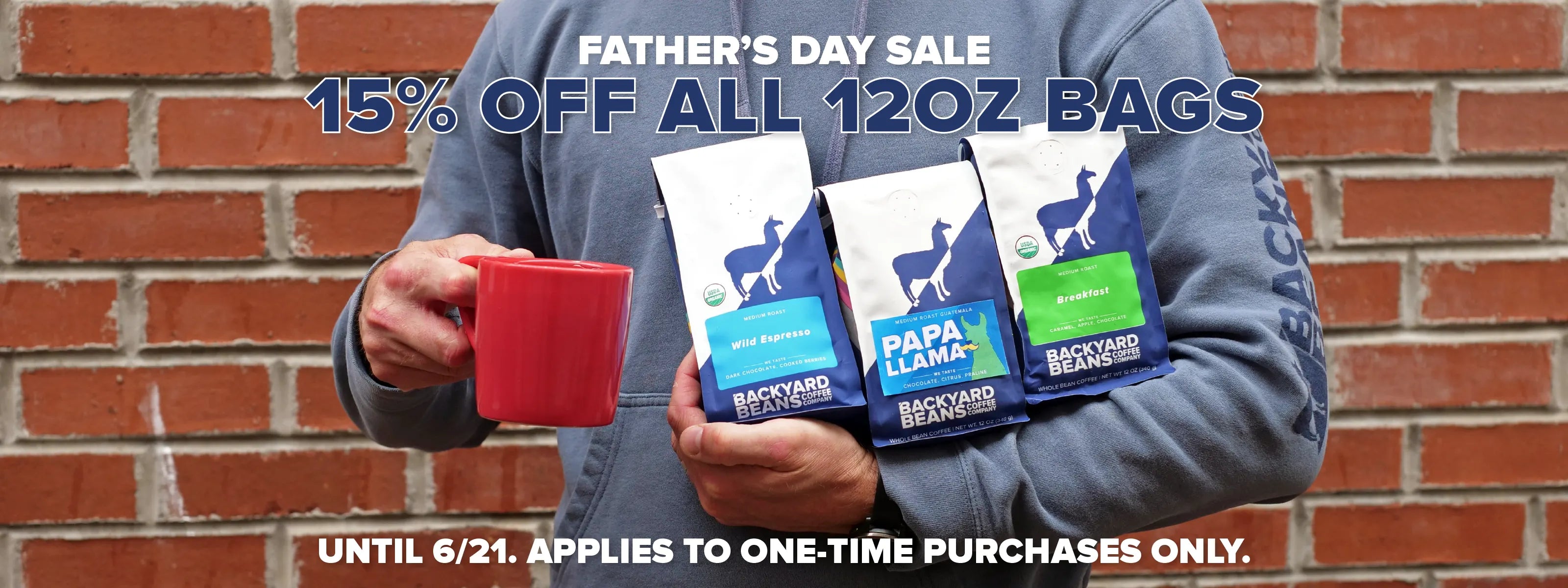 Person holding retail coffee bags and a mug with Father's Day sale text against a brick wall.