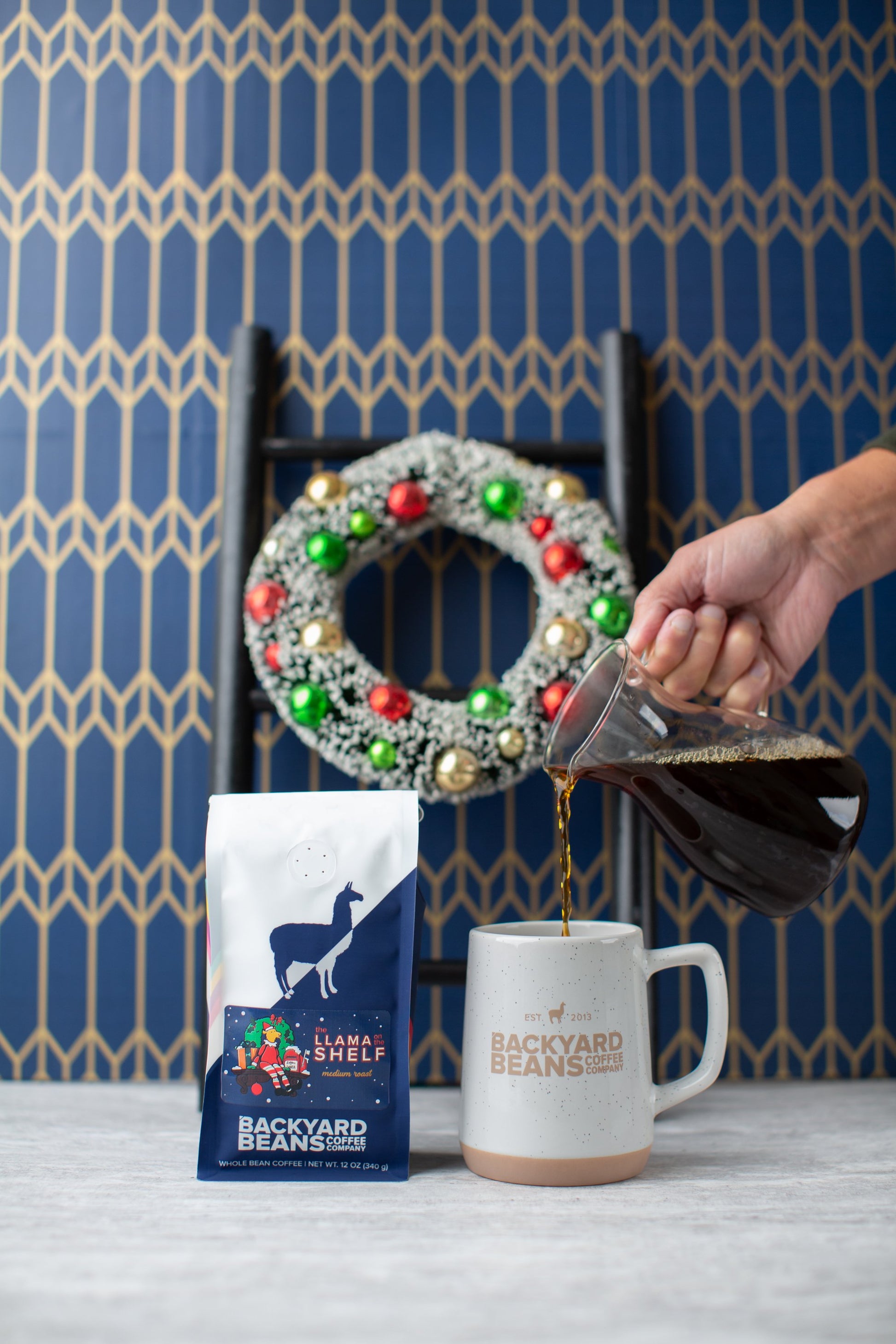 Image of hand pouring coffee into mug with a Llama on the Shelf coffee bag.
